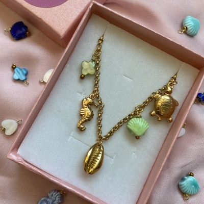 Colar dourado com pendentes marinhos em caixa rosa sobre tecido rosa