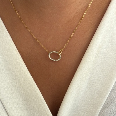 Colar dourado com pendente ovalado cravejado de pedras brancas em decote branco