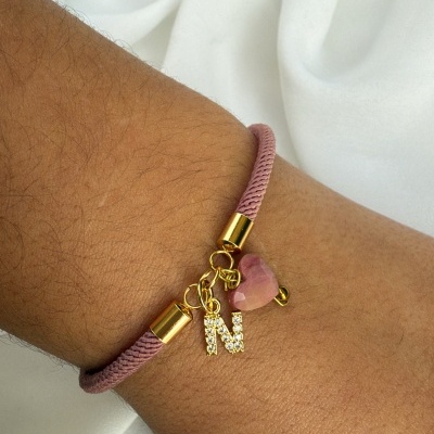 Pulseira cor-de-rosa com pendentes dourados e letra N no pulso