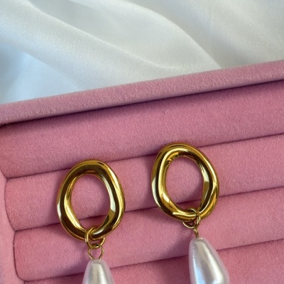 Brincos dourados com pendente de pérola numa caixa rosa