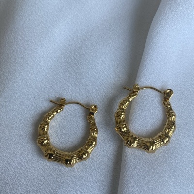 Brincos argola dourados com textura de bambu sobre tecido branco