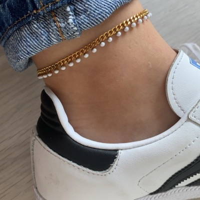 Tornozeleira dourada com contas brancas no tornozelo, calça de ganga e sapatilha branca