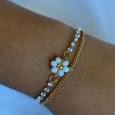 Pulseira dourada com pedras brancas em formato de flor num pulso.