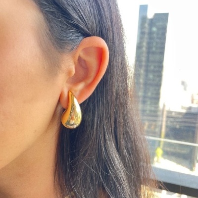 Brincos dourados em forma de gota na orelha de mulher com cabelo preto