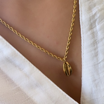 Colar dourado com pendente de concha numa camisa branca com botão castanho