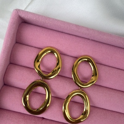 Brincos dourados ovalados sobre suporte rosa acolchoado
