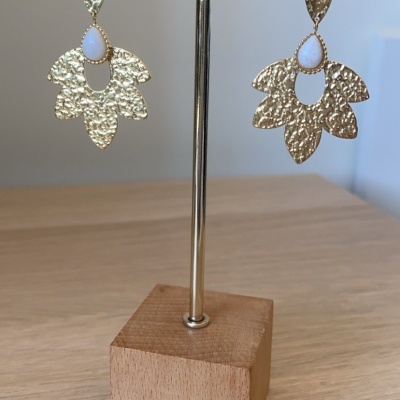 Brincos dourados com pedra branca pendurados em suporte de madeira