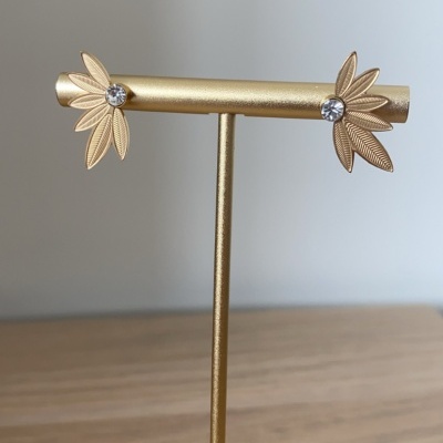 Brincos dourados em forma de folhas com pedras transparentes no centro, mostrados num suporte dourado