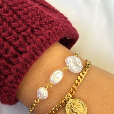 Pulseiras douradas com pérolas e pendente de moeda num pulso com camisola vermelha