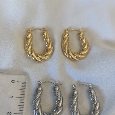 Quatro pares de brincos argola torcidos dourados e prateados sobre tecido branco com régua ao lado