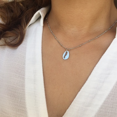 Colar prateado com pendente oval com desenho de folha usado com camisa branca