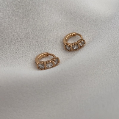 Brincos de ouro com três pedras brilhantes sobre tecido branco