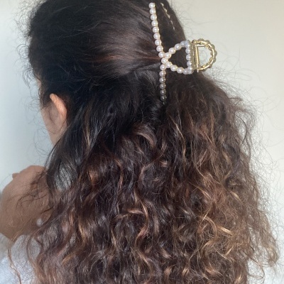 Presilha de cabelo de pérolas brancas com estrutura dourada em cabelo cacheado castanho