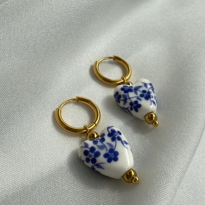 Brincos dourados com pendente de coração branco com padrão floral azul