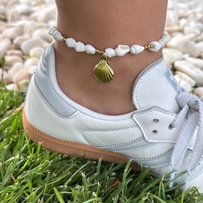 tornozeleira com pedras brancas e pendente de concha dourada junto a sapatilha branca no relvado