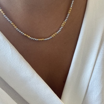 Colar delicado dourado e prateado sobre pele e roupa branca