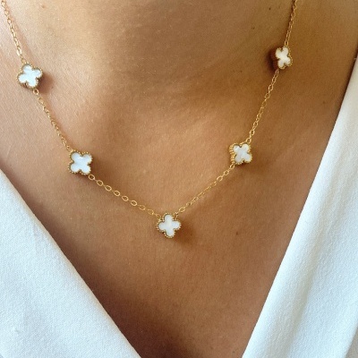 Colar com cinco flores brancas em corrente dourada, usado sobre pele clara.