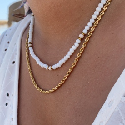 Colares branco e dourado no pescoço de pessoa com roupa branca bordada