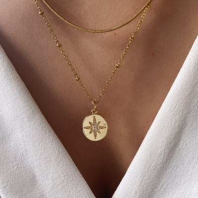 Colar dourado com pendente redondo e estrela de oito pontas com pedras sobre tecido branco
