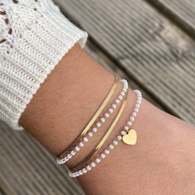 Pulseiras douradas e brancas no pulso com pendente de coração