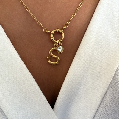 Colar dourado com pendente letra S e coração de pedra sobre roupa branca