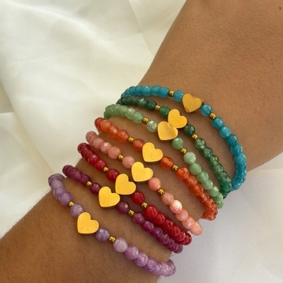 Pulseiras coloridas com corações dourados num pulso sobre tecido branco