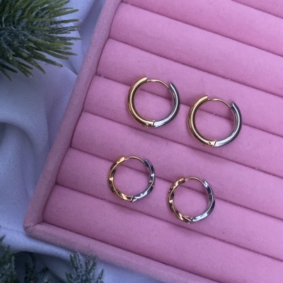 Dois pares de brincos de argola bicolores em caixa de veludo rosa com elementos naturais ao lado