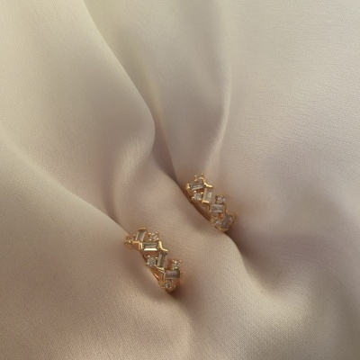 Brincos dourados com pedras transparentes sobre tecido branco