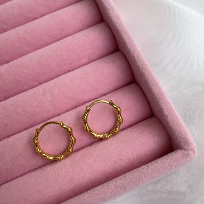 Brincos dourados em caixa de veludo rosa sobre tecido branco