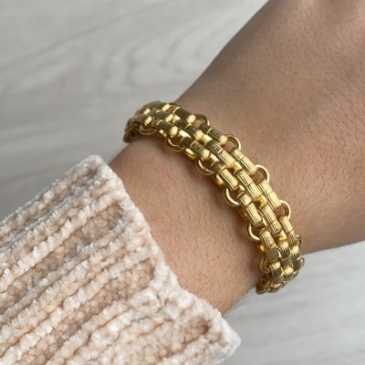 Pulseira dourada entrelaçada no pulso com camisola creme texturada