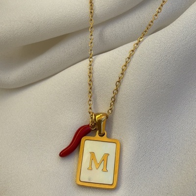 Colar dourado com pendente retangular branco com a letra M dourada e pendente vermelho em forma de pimento
