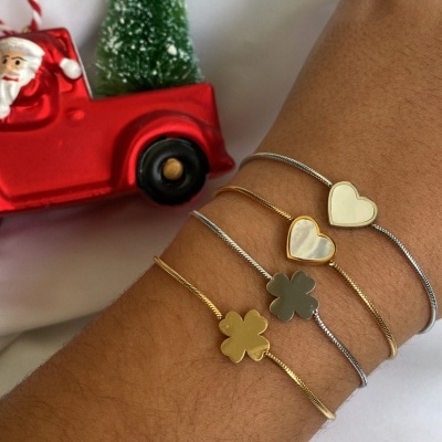 Pulseras douradas e prateadas com pendentes de coração e trevo num pulso junto de decoração natalícia