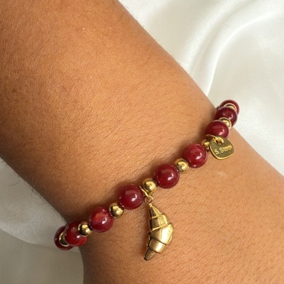 Pulseira vermelha e dourada com pendente em forma de croissant no pulso