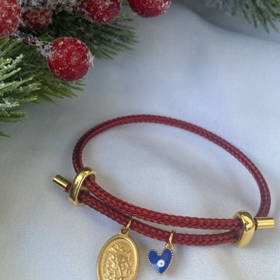 Pulseira vermelha com medalhão dourado e coração azul pendurados perto de ramos de pinheiro e bagas vermelhas artificiais