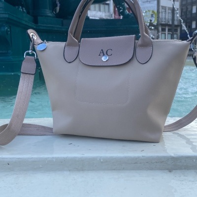 Mala de mão bege com alças e correia castanha junto a fonte com estátuas negras de cavalos alados