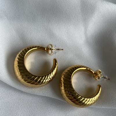 Brincos dourados em argola com textura sobre tecido branco