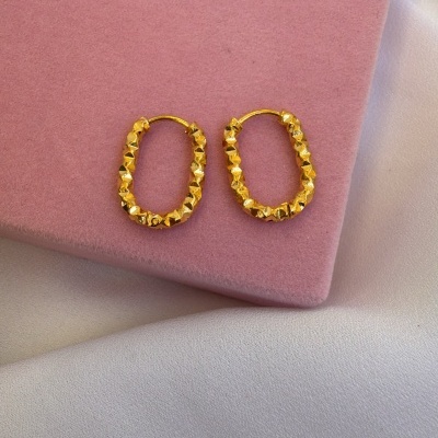 Brincos dourados ovalados com textura facetada sobre superfície rosa aveludada