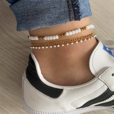 Tornozelo com pulseiras douradas e brancas, jeans azul e ténis branco com detalhes pretos