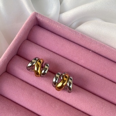 Brincos bicolores de metal numa caixa rosa de veludo sobre fundo branco.