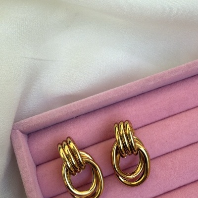 Brincos dourados em caixa de veludo rosa sobre tecido branco