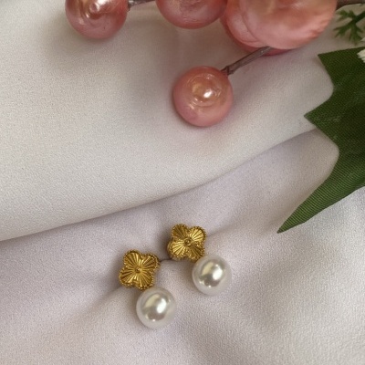 Brincos dourados em forma de flor com pérolas brancas, sobre tecido branco com decoração floral rosa e verde