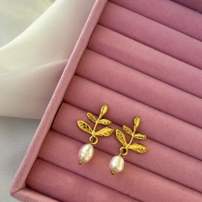 Brincos dourados com pérolas em caixa rosa sobre tecido branco