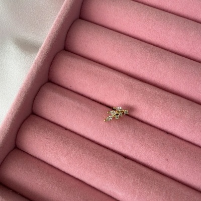 Pequena joia dourada com pedras sobre almofada rosa