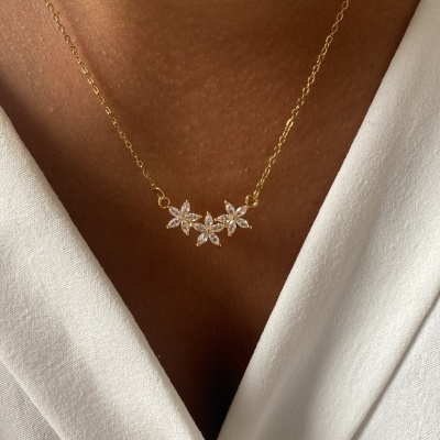 Colar dourado com três flores prateadas e brilhantes no pescoço