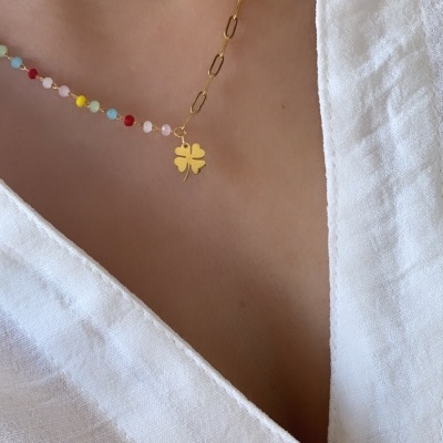 Colar dourado com pendente de trevo e cristais coloridos numa pessoa com camisa branca