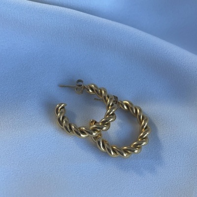 Brincos dourados em argola torcido sobre tecido azul claro