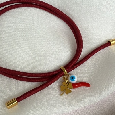 Pulseira vermelha com pendentes dourado, olho azul e chifre vermelho sobre tecido branco
