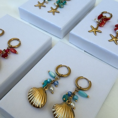 Brincos dourados com pingentes de estrela-do-mar e concha em suportes brancos.