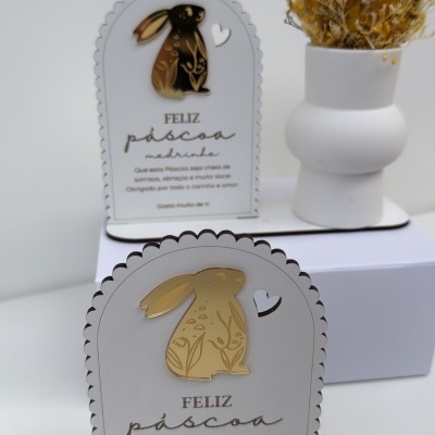 Placas decorativas de Páscoa com coelhos dourados e texto em português em fundo branco com vaso e flores secas ao fundo
