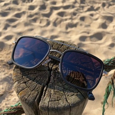 Óculos de sol pretos com lentes escuras numa praia sobre um poste de madeira.